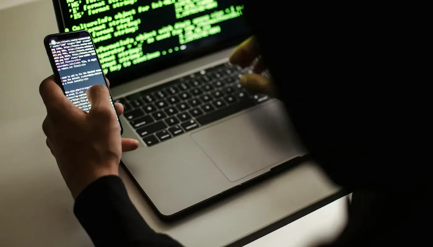 An unrecognizable programmer working with a laptop and smartphone